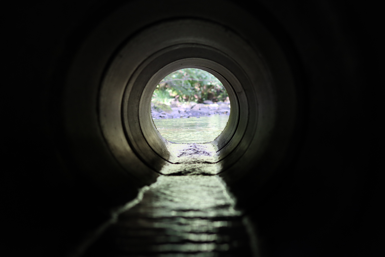 View through a round concrete tunnel carrying a stream beneath a road